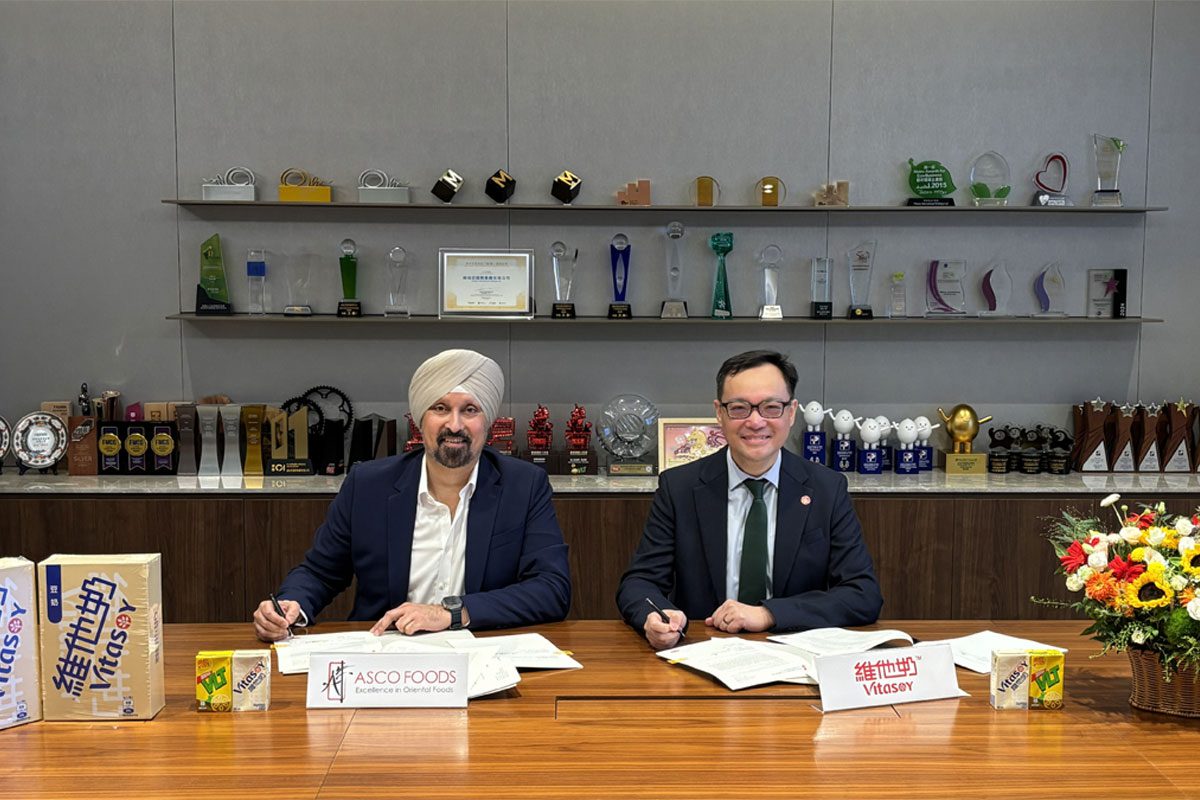 Representatives from Asco Foods and Vitasoy sit at a table signing a new distribution deal between the two firms.
