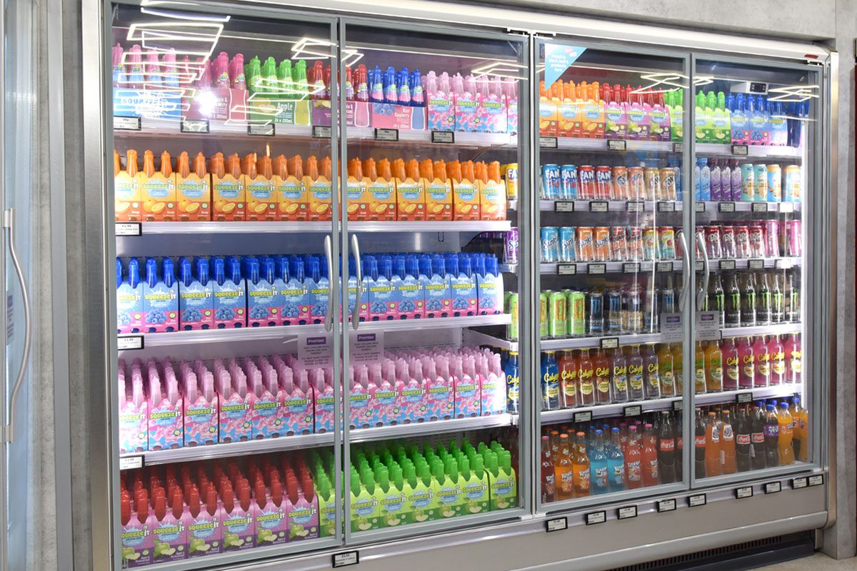 An image of a refrigerator unit inside a convenience store with soft drinks inside and doors on the chiller.