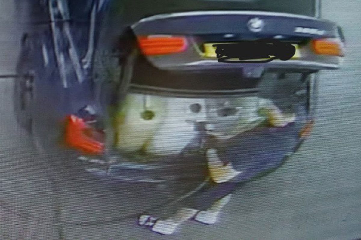 A man fills up plastic containers in the boot of his car with fuel.