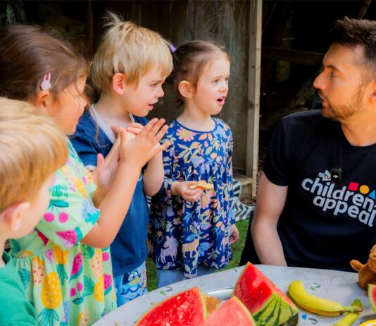 Kellogg’s teams up with STV’s Big Scottish Breakfast STV presenter Sean Batty sits at a table with fruit on it talking to a group of children.
