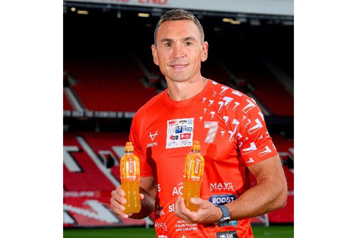 Sir Kevin Sinfield stands holding bottles of Boost Sport drinks while standing in Old Trafford stadium.