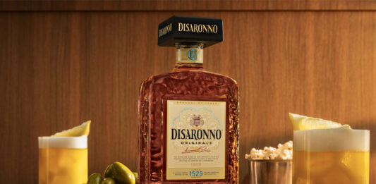 Disaronno unveils new bottle design A bottle of the 2026 redesign for Disaronno stands on a table with Amaretto Sour cocktail serves around it as well as bowls of nibbles.