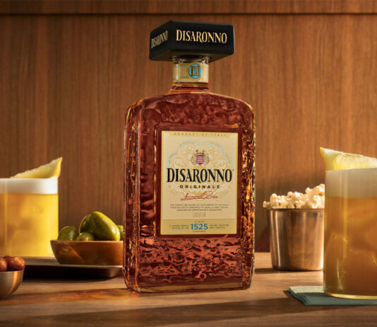 Disaronno unveils new bottle design A bottle of the 2026 redesign for Disaronno stands on a table with Amaretto Sour cocktail serves around it as well as bowls of nibbles.