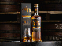 Glasgow 1770 unveils first 10 Year Old peated malt A bottle of Glasgow 1770 10 Year Old Peated Single Malt Scotch Whisky stands on a barrel with its outer packaging next to it with a nosing glass with the whisky inside.