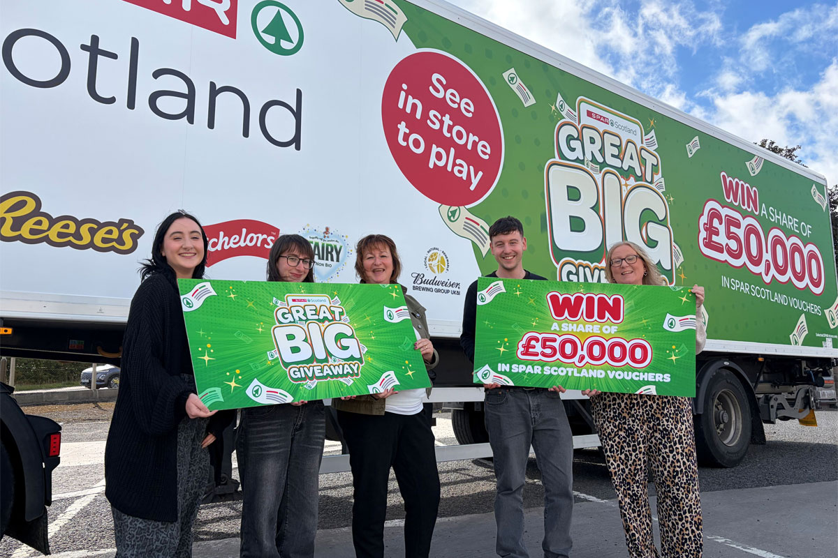 Members of the Spar Scotland team hold banners for the Great Big Giveaway promotion while standing in front of a Spar Scotland delivery truck with the campaign's livery across it.