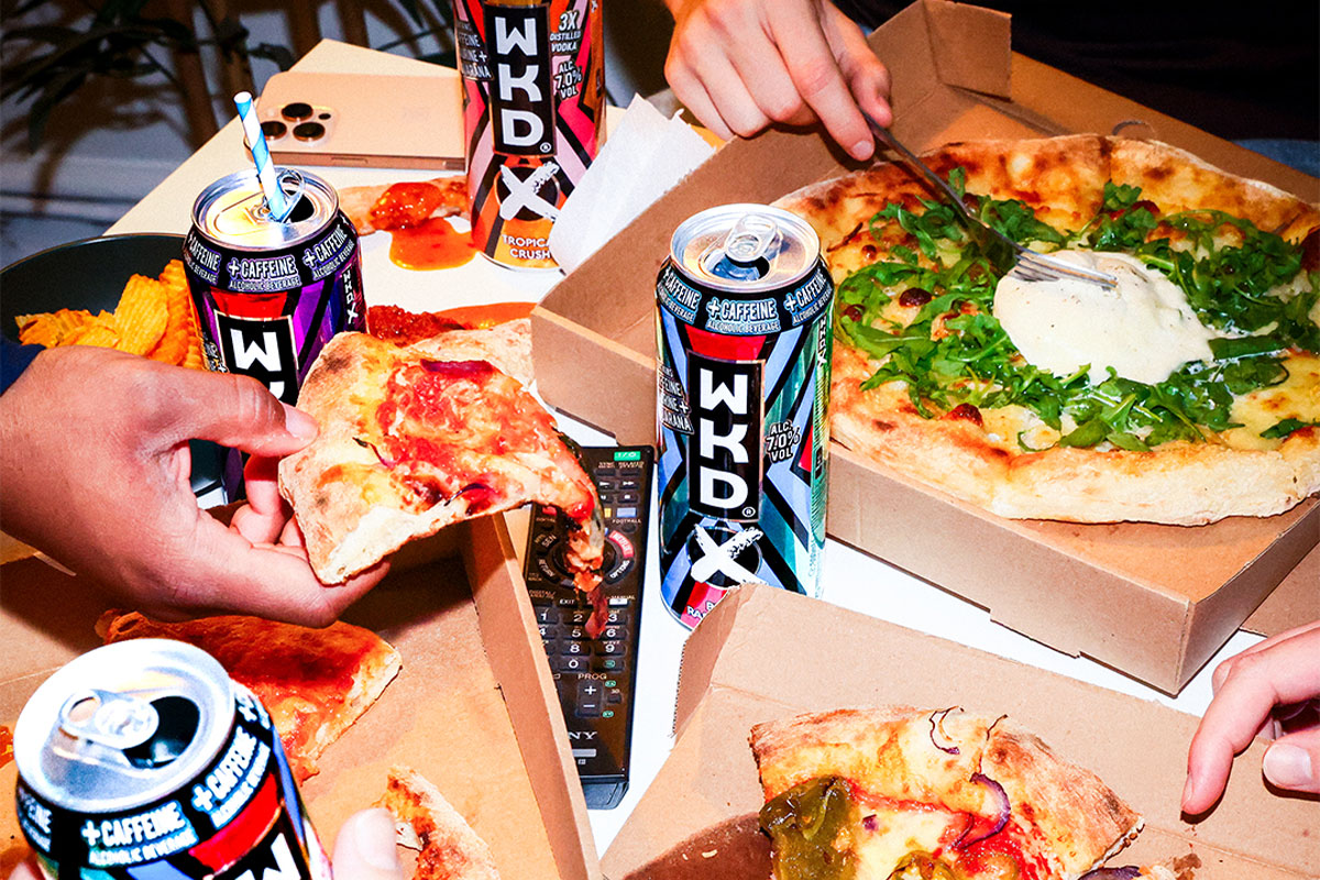 A group of people are taking slices of pizza from different boxes with cans of WKDX around the boxes.