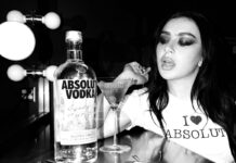 Absolut Vodka teams up with Charli XCX Pop star Charli XCX sits at a dressing table with a Dirty Martini cocktail serve next to a bottle of Absolut Vodka. The photo is in black and white.