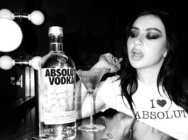 Absolut Vodka teams up with Charli XCX Pop star Charli XCX sits at a dressing table with a Dirty Martini cocktail serve next to a bottle of Absolut Vodka. The photo is in black and white.