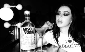 Absolut Vodka teams up with Charli XCX Pop star Charli XCX sits at a dressing table with a Dirty Martini cocktail serve next to a bottle of Absolut Vodka. The photo is in black and white.