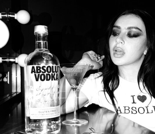 Absolut Vodka teams up with Charli XCX Pop star Charli XCX sits at a dressing table with a Dirty Martini cocktail serve next to a bottle of Absolut Vodka. The photo is in black and white.