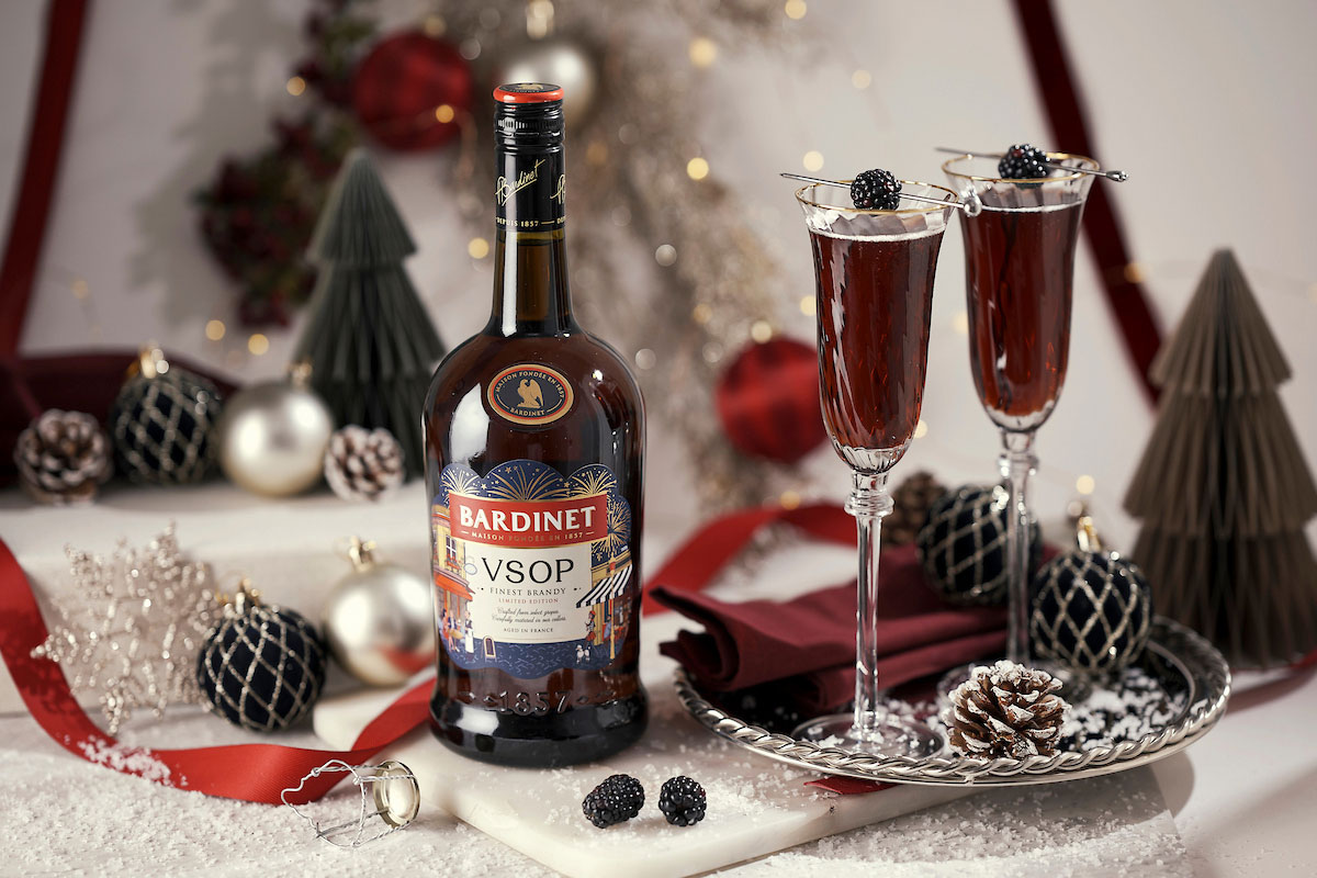 A bottle of Bardinet VSOP stands on a table with two cocktail serves next to it. There is a range of Christmas decorations across the table as well.