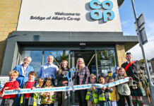 Co-op opens its doors in Bridge of Allan A group of people stand outside Co-op Bridge of Allan holding novelty scissors and cutting a Co-op branded ribbon as part of the store's opening ceremony.