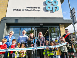 Co-op opens its doors in Bridge of Allan A group of people stand outside Co-op Bridge of Allan holding novelty scissors and cutting a Co-op branded ribbon as part of the store's opening ceremony.