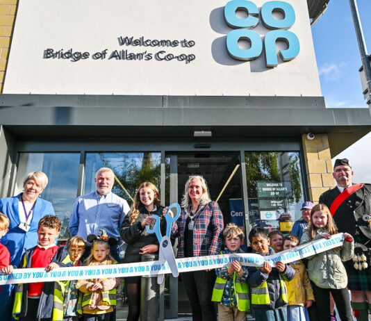 Co-op opens its doors in Bridge of Allan A group of people stand outside Co-op Bridge of Allan holding novelty scissors and cutting a Co-op branded ribbon as part of the store's opening ceremony.