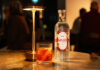 Eden Mill unveils Winter gin for Negroni cocktails A bottle of Eden Mill Winter in St Andrews gin stands on a table with a Negroni cocktail serve next to it and a lamp.