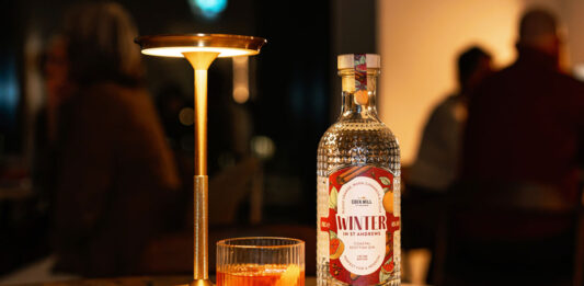 Eden Mill unveils Winter gin for Negroni cocktails A bottle of Eden Mill Winter in St Andrews gin stands on a table with a Negroni cocktail serve next to it and a lamp.
