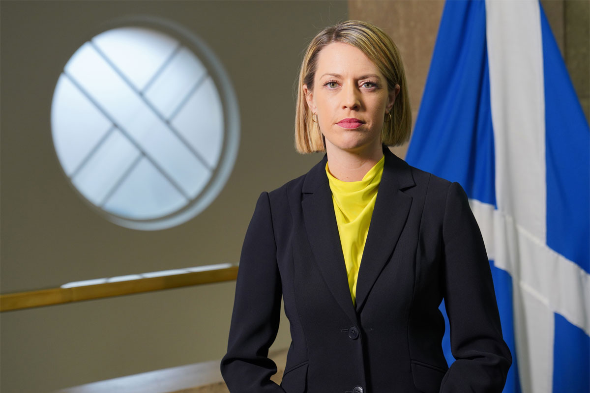 Jenny Gilruth, deputy First Minister of the Scottish Government, stands in Parliament with the Scotland flag behind her.