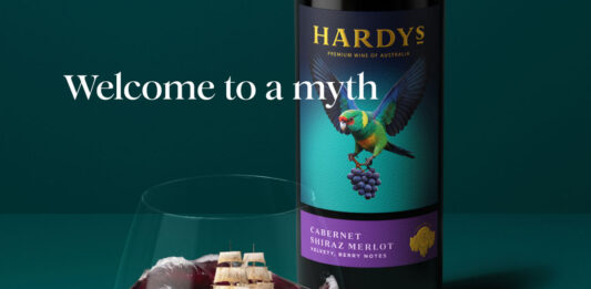 Hardys wine unveils complete brand refresh Promotional image of the new Hardys wine redesign with a bottle of the wine in the background with a glass of red wine poured in front of it. The wine inside mimics a stormy sea with a ship in the tides. The text around the two reads 'Welcome to a myth you can pour'.