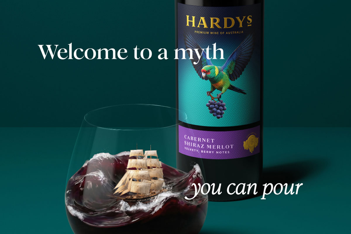 Promotional image of the new Hardys wine redesign with a bottle of the wine in the background with a glass of red wine poured in front of it. The wine inside mimics a stormy sea with a ship in the tides. The text around the two reads 'Welcome to a myth you can pour'. 