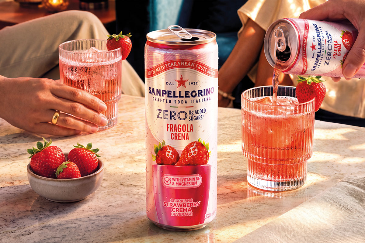 A can of Sanpellegrino Zero Strawberry Crema stands on a table with glasses with the drink inside them behind it and a bowl of strawberries next to it.