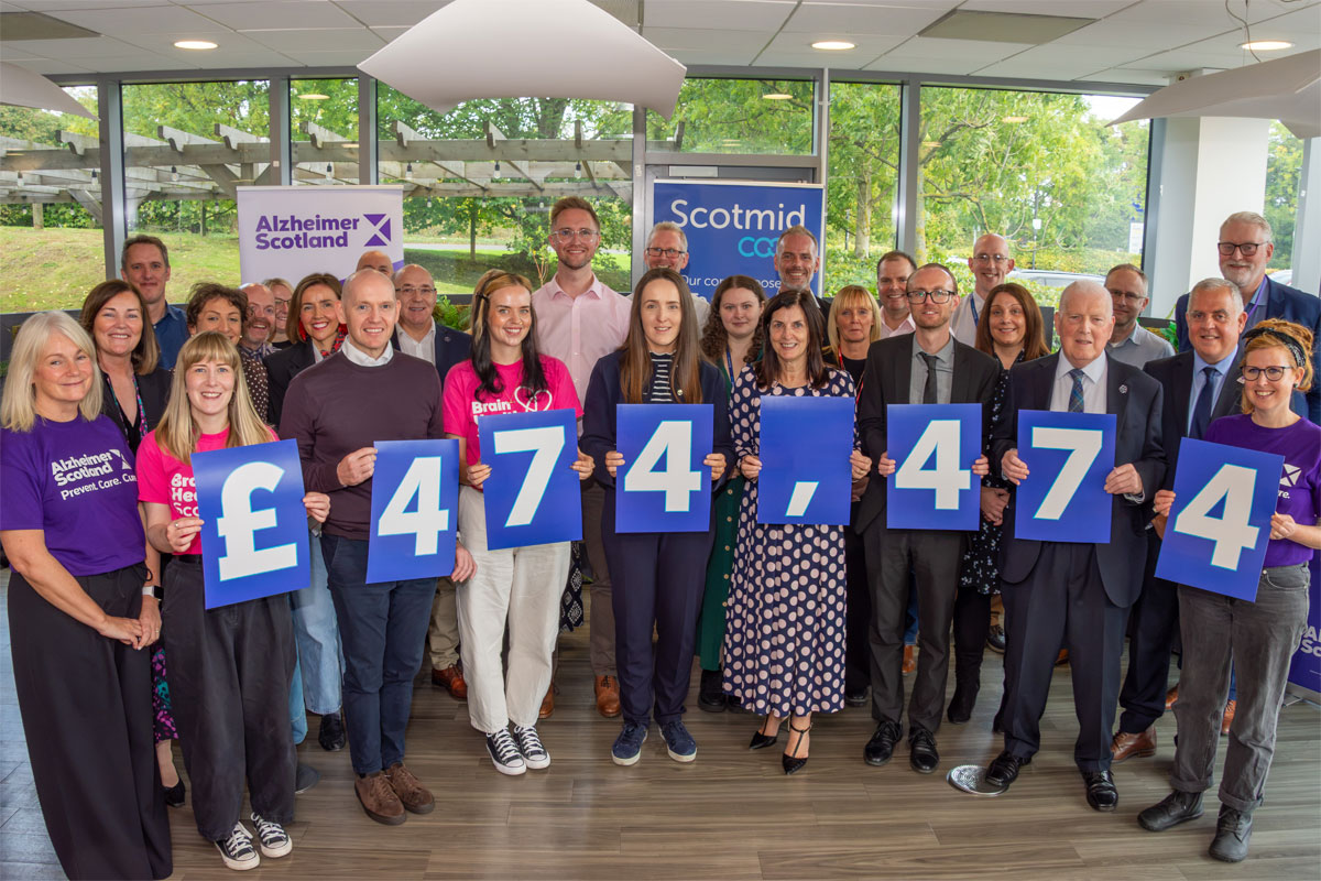 Members of the Scotmid Co-op and Alzheimer Scotland teams stand together holding signs that read £474,474 to highlight the fundraising the retail chain has made for the charity.