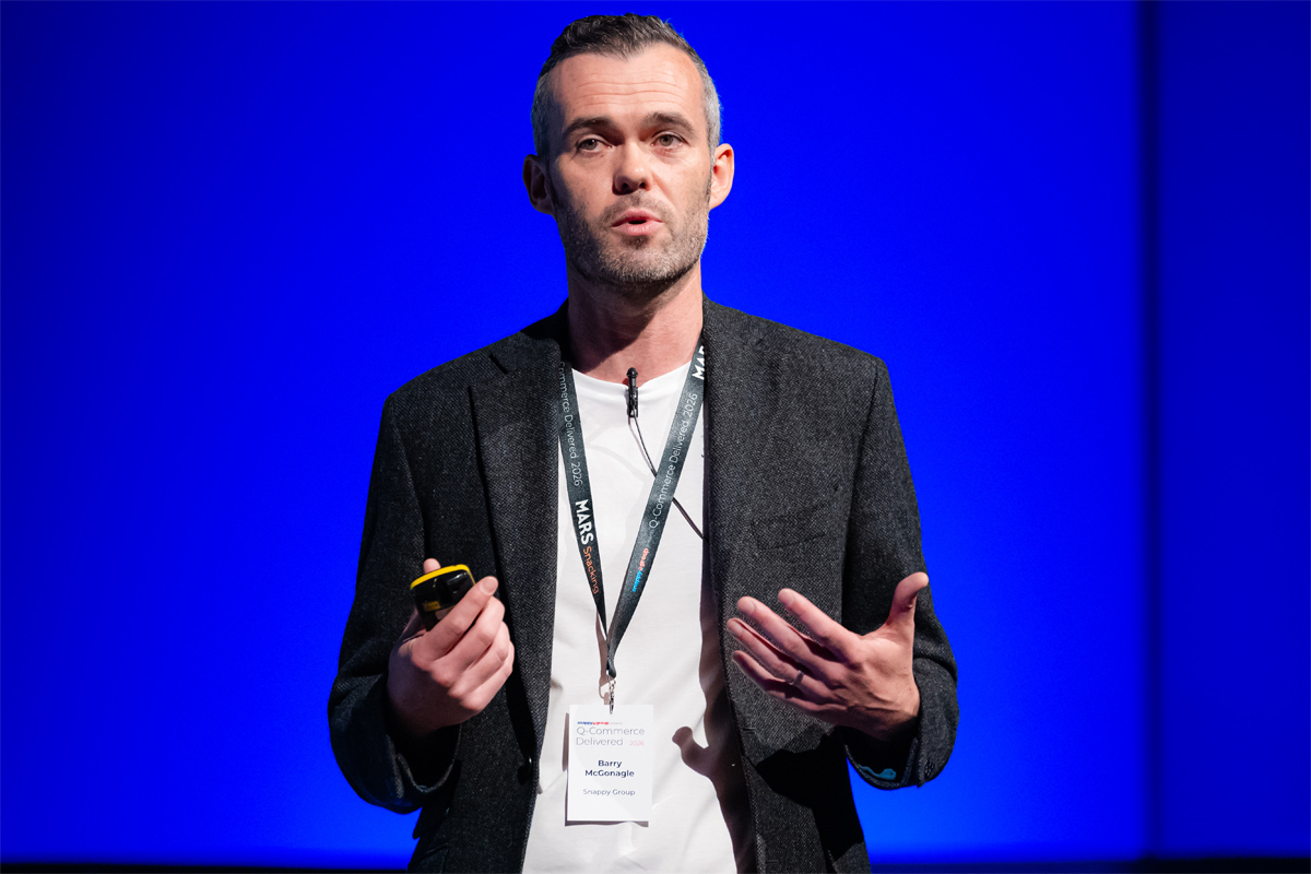 Barry McGonagle, chief financial officer at Snappy Group, stands on a stage with a blue backdrop delivering a talk.